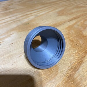 May include: A grey plastic 3D printed ring with a hole in the centre. The ring has a textured surface and appears to be part of a larger object.
