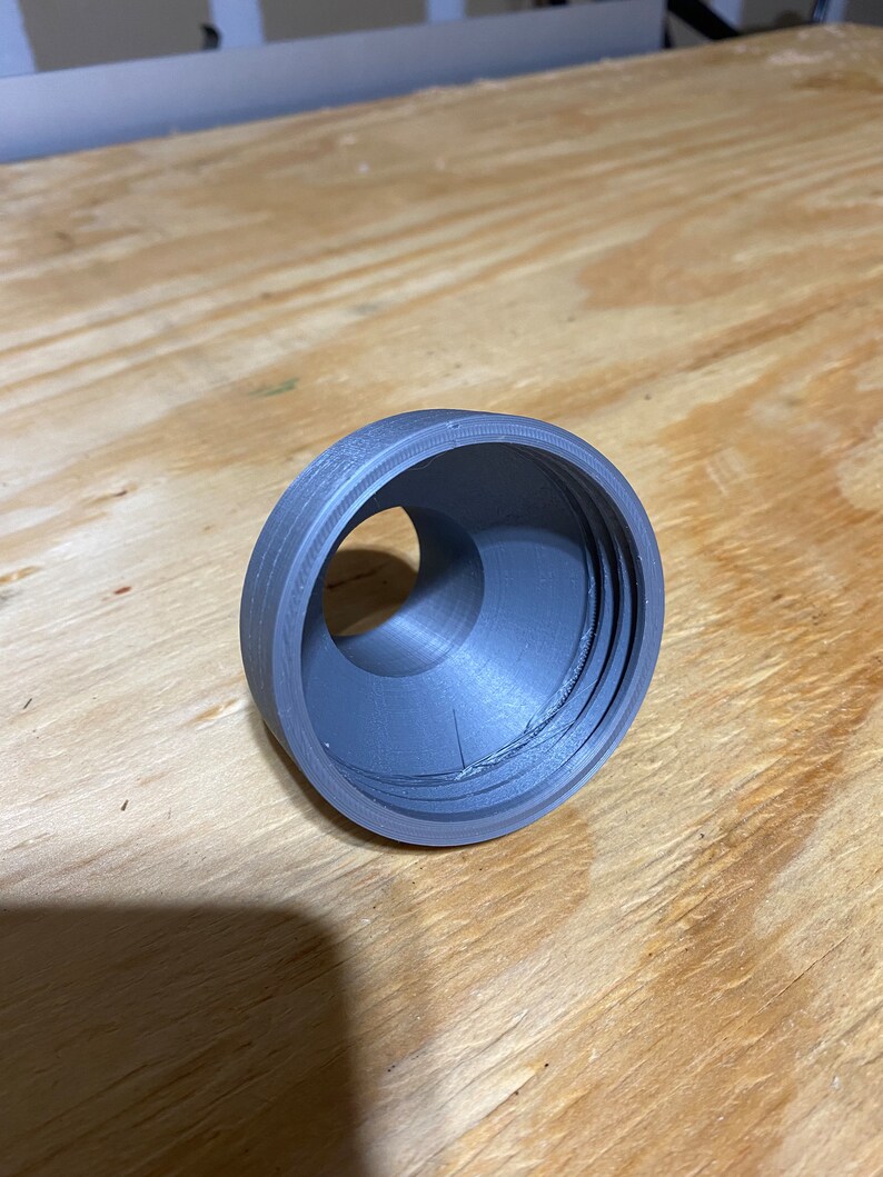 May include: A grey plastic 3D printed ring with a hole in the centre. The ring has a textured surface and appears to be part of a larger object.
