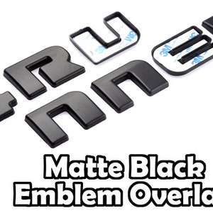 May include: Matte black emblem overlay letters. The letters are in a sans-serif font and are shown on a white background. The letters have adhesive backing. The text "Matte Black Emblem Overlay" is shown in a black and white font.