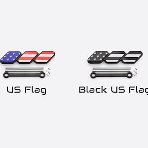 Może przedstawiać: Dwa emblematy z wzorem flagi USA i czarnym wzorem flagi USA. Każdy emblemat ma trzy połączone sekcje. Tekst "US Flag" i "Black US Flag" znajdują się poniżej. Każdy emblemat ma czarną podstawę ze srebrnym osprzętem.