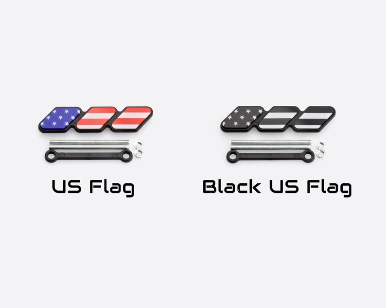 Może przedstawiać: Dwa emblematy z wzorem flagi USA i czarnym wzorem flagi USA. Każdy emblemat ma trzy połączone sekcje. Tekst "US Flag" i "Black US Flag" znajdują się poniżej. Każdy emblemat ma czarną podstawę ze srebrnym osprzętem.