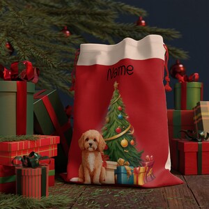 May include: Red Christmas gift bag with a white top and red drawstring. The bag features a Christmas tree and a cute puppy illustration. The word "Name" is printed on the bag. Presents and a Christmas tree are in the background.