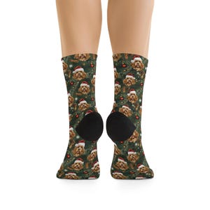 K&ouml;nnte beinhalten: Socken mit einem sich wiederholenden Muster eines braunen Hundes mit Weihnachtsm&uuml;tze, vor einem Hintergrund aus gr&uuml;nen Weihnachtsbaumzweigen, roten Kugeln und Zimtstangen. Die Socken werden an den Beinen einer Person getragen.