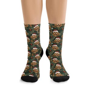 K&ouml;nnte beinhalten: Socken mit einem sich wiederholenden Muster eines Hundes mit Weihnachtsm&uuml;tze, roten Ornamenten und Zimtstangen auf dunklem Gr&uuml;n. Die Socken haben schwarze Fersen und Zehen.
