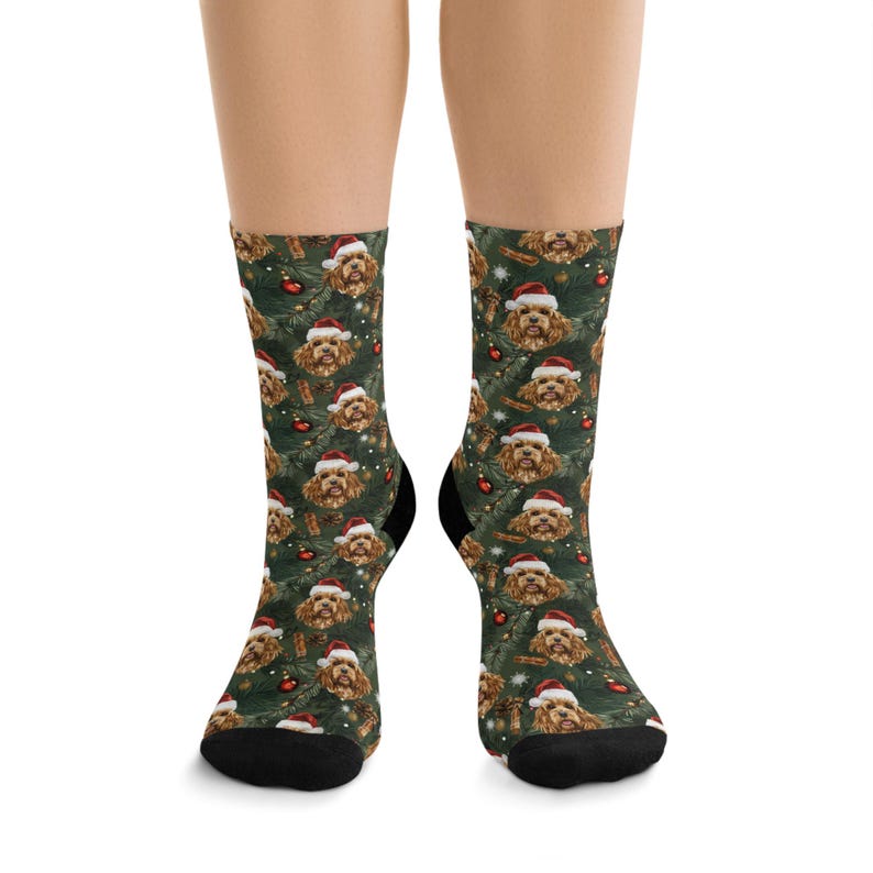 K&ouml;nnte beinhalten: Socken mit einem sich wiederholenden Muster eines Hundes mit Weihnachtsm&uuml;tze, roten Ornamenten und Zimtstangen auf dunklem Gr&uuml;n. Die Socken haben schwarze Fersen und Zehen.