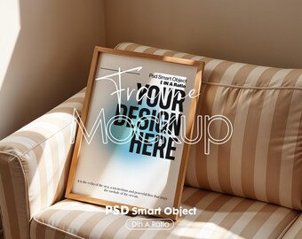May include: A wooden frame mockup with a light blue and white gradient background. The text "Frame Your Design Here" is written in black on the background. The frame is sitting on a striped couch.