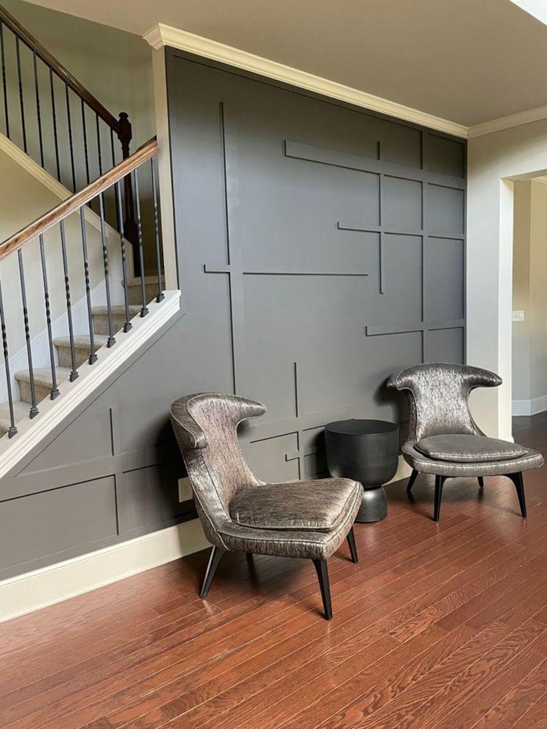 May include: Two chairs with a silver fabric upholstery and black legs sit in front of a gray wall with a geometric design. A black side table sits between the chairs.