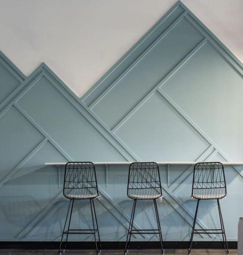 May include: Three black metal chairs with a geometric wire design sit in front of a light blue wall with a geometric pattern. The wall is made of wood panels.