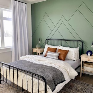 May include: A black metal bed frame with a white and gray patterned duvet and a gray throw blanket. The bed is in a bedroom with a green wall featuring a geometric pattern.