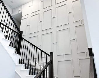 May include: A white wall with a geometric pattern of raised squares and rectangles. A black metal railing with vertical spindles leads up a set of white stairs with a grey carpet runner.