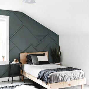May include: A wooden bed frame with a gray and white patterned blanket and pillows. The bed is in a bedroom with a dark green wall with geometric shapes.