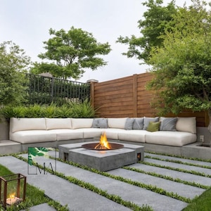 May include: An outdoor seating area with a concrete fire pit and a burning fire. A cream-coloured sectional sofa with cushions and pillows is set against a wooden fence. The area includes a lawn and trees.