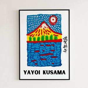 May include: A framed art print featuring a colorful illustration of a mountain with a red and yellow peak, green trees, and blue water. The sky is blue with white dots and a red sun. The artist's name, Yayoi Kusama, is printed at the bottom.