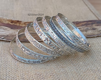 May include: Set of six silver bangles with intricate floral and geometric designs. The bangles are stacked on top of each other, showcasing their unique patterns.