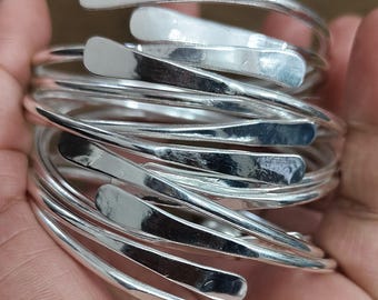 Puede incluir: Un conjunto de pulseras de plata, cada una con una forma y un ancho ligeramente diferentes, apiladas unas sobre otras.