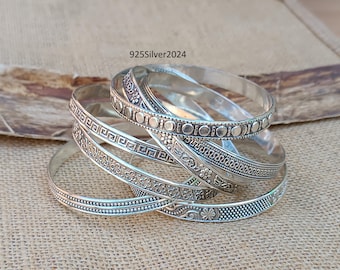 May include: Set of six silver bangles with intricate etched designs. The bangles are stacked on top of each other, showcasing the different patterns.