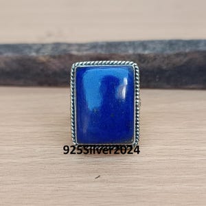 May include: A silver ring with a rectangular blue lapis lazuli gemstone set in a rope-like border.