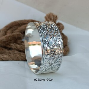 May include: A silver bangle bracelet featuring a floral design. The bracelet is crafted from 925 sterling silver and has a polished finish.