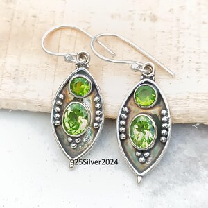 May include: A pair of sterling silver earrings with a drop design. Each earring features two oval-cut, light green gemstones. The earrings have a hook closure and are embellished with small silver beads. The text "925Silver2024" is visible.