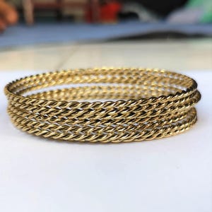 Puede incluir: Cuatro pulseras de metal retorcido de color dorado apiladas unas sobre otras.
