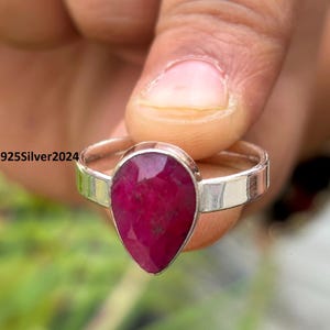 Puede incluir: Un anillo de plata con una piedra preciosa roja oscura en forma de pera. El anillo tiene una banda de plata pulida. El texto "925Silver2024" es visible en el anillo.