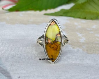 May include: A silver ring with an oval-shaped stone. The stone has a mix of yellow, orange, and brown colours with copper accents. The ring is set on a white surface. The text "925Silver2024" is visible on the ring.