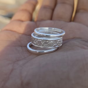 May include: Four silver rings stacked on top of each other. The top ring has a floral design.