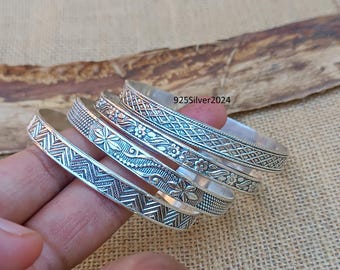 May include: Set of five silver bangles with intricate floral and geometric designs. The bangles are stacked on top of each other, showcasing the different patterns.