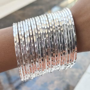 May include: A stack of silver hammered metal bangles. The bangles are stacked on a person's wrist.