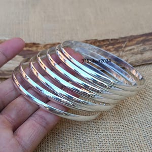 May include: A set of seven silver bangles stacked on top of each other. The bangles are smooth and shiny, and they are all the same width.