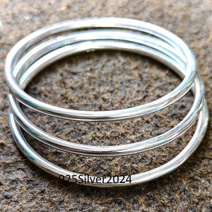 Peut inclure: Quatre bracelets en argent empilés les uns sur les autres. Les bracelets sont lisses et brillants.