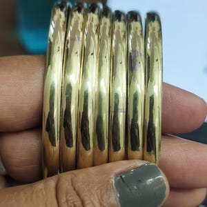 Op de afbeelding: Een stapel van zes gouden armbanden, elk met een glad, afgerond oppervlak.