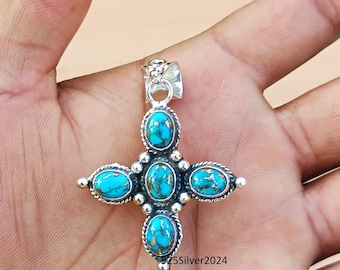 May include: A silver cross pendant with oval turquoise stones. The stones are set in a silver frame with a rope-like border. The pendant has a loop at the top for a chain. The text "925Silver2024" is visible.