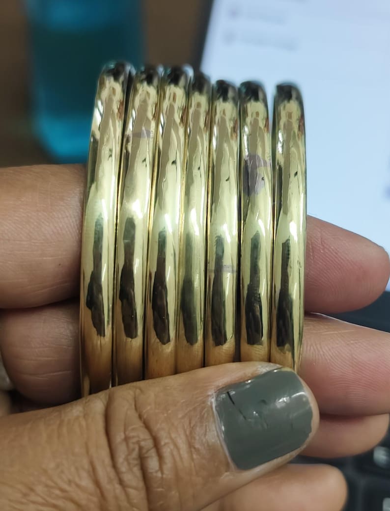 Op de afbeelding: Een stapel van zes gouden armbanden, elk met een glad, afgerond oppervlak.