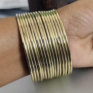 Peut inclure: Un ensemble de bracelets dorés, portés au poignet.