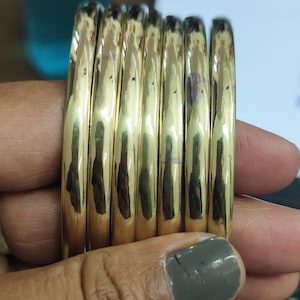 Op de afbeelding: Een stapel van zes gouden armbanden, elk met een glad, afgerond oppervlak.