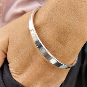 Puede incluir: Un brazalete de plata con un acabado liso y pulido.