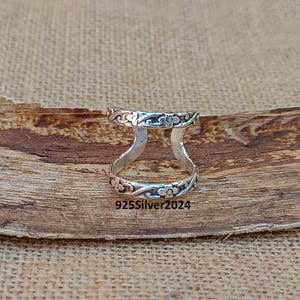 May include: A silver ring with a floral design. The ring is open on both sides and features a delicate floral pattern.