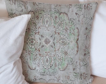 Puede incluir: Una silla de mimbre con una variedad de almohadas blancas y una almohada estampada con un diseño verde, marrón y blanco.