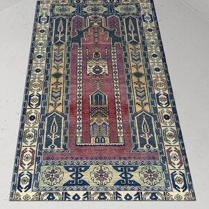 Könnte beinhalten: Ein traditioneller türkischer Gebetsteppich in Rot, Blau und Creme. Der Teppich zeigt komplizierte geometrische Muster und florale Motive.