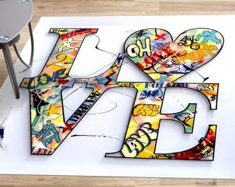 Puede incluir: Un fondo blanco con un contorno negro de la palabra "LOVE" en letras grandes y en negrita. Las letras están llenas de diseños y palabras de estilo graffiti coloridos, que incluyen "OH", "FREE", "FOLLOW" y "LOVE". Una forma de corazón está incorporada en la letra "O".