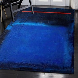 May include: A rectangular rug with an abstract design. The rug features a gradient of blues, from deep navy to bright blue, with a thin red line across the top. The texture appears to be rough and textured.
