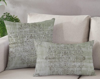 Puede incluir: Dos almohadas decorativas con un esquema de color verde y gris descolorido. Las almohadas presentan un patrón repetido de un diseño de mandala en blanco y negro.