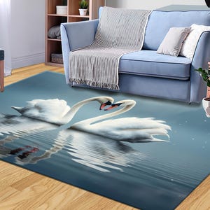 Könnte beinhalten: Ein blauer und weißer Teppich mit einem Design aus zwei weißen Schwänen, deren Hälse ineinander verschlungen sind und eine Herzform bilden. Die Schwäne spiegeln sich im Wasser unter ihnen.