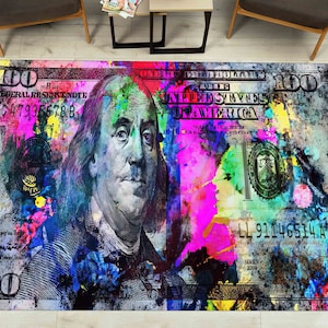 May include: A colourful abstract rug featuring a large image of a $100 bill with Benjamin Franklin's portrait. The bill is covered in splashes of paint in various colours, including pink, blue, green, and yellow.