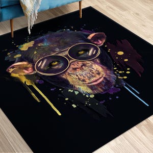 May include: A black rug featuring an abstract design of a monkey wearing sunglasses. The monkey's fur is purple, blue, and yellow, and the sunglasses are gold.