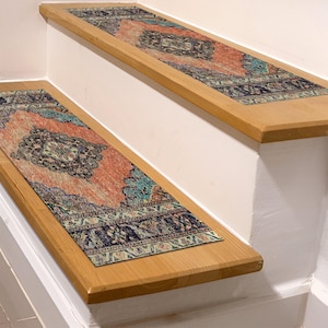 May include: Stair treads with an ornate, vintage-style design. The treads feature a central medallion pattern in shades of coral, teal, and navy blue, bordered by a detailed navy blue pattern. The treads are placed on wooden stairs.
