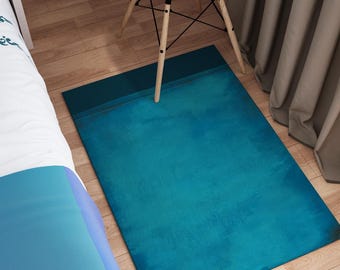 May include: A teal blue rug with a subtle distressed texture. The rug is placed on a wooden floor in a room with a white chair and curtains.