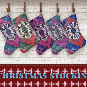 Pode incluir: Cinco meias de Natal coloridas com padrões intrincados penduradas em uma parede de tijolo branco. As meias são feitas de tecido e têm um design tradicional turco kilim.
