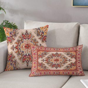 May include: Two decorative throw cushions with a beige backdrop and a detailed, colourful pattern. The square and rectangular cushions feature a traditional rug design with red, blue, yellow, and orange accents, adding elegance to any living space.